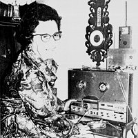 Schwarz-Weiß-Foto eines Mannes an einem historischen Tonbandgerät und weiteren Audiogeräten